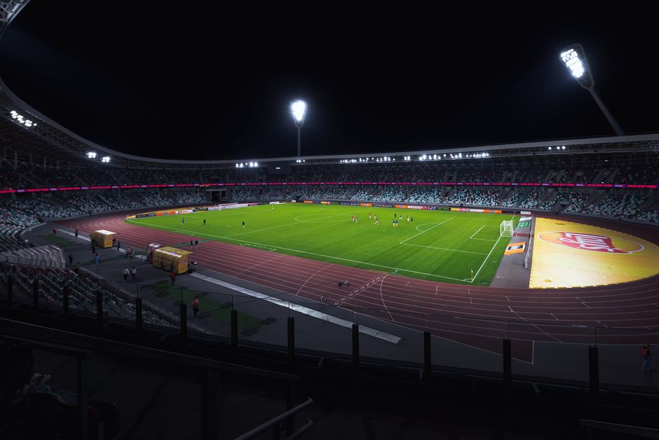 Brightly lit empty soccer stadium with green field under spotlights during night time.